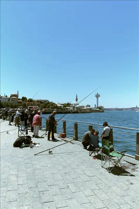 İstanbul Boğazı kıyısında güneşli bir günde olta balıkçılığı yapan insanlar ve arka planda tarihi yarımada.
