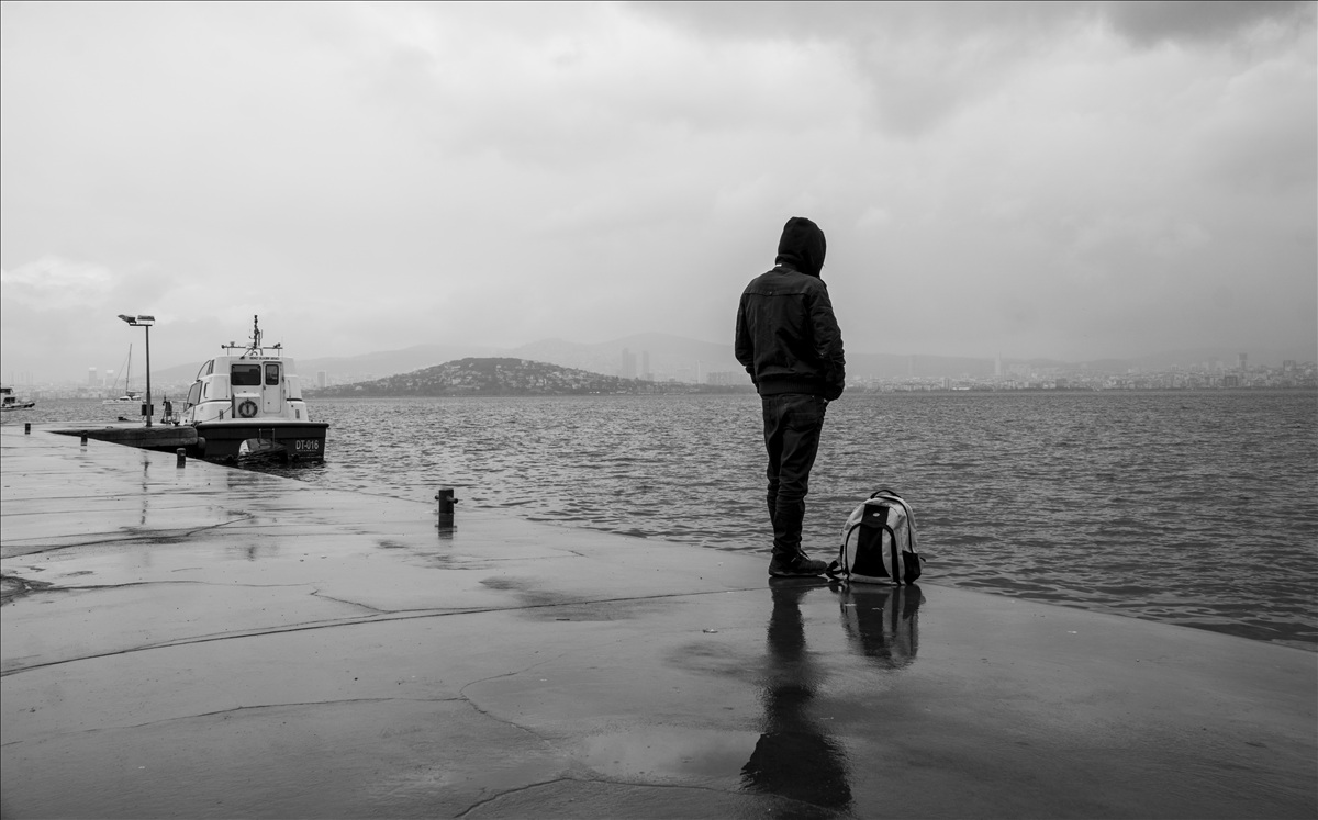 Yağmurlu havada adalar'da sırt çantasıyla denizi izleyen yalnız adam ve iskelede tekne manzarası